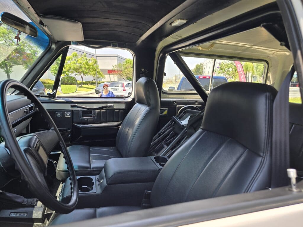 Interior view of a classic car with black leather seats and a roll cage.