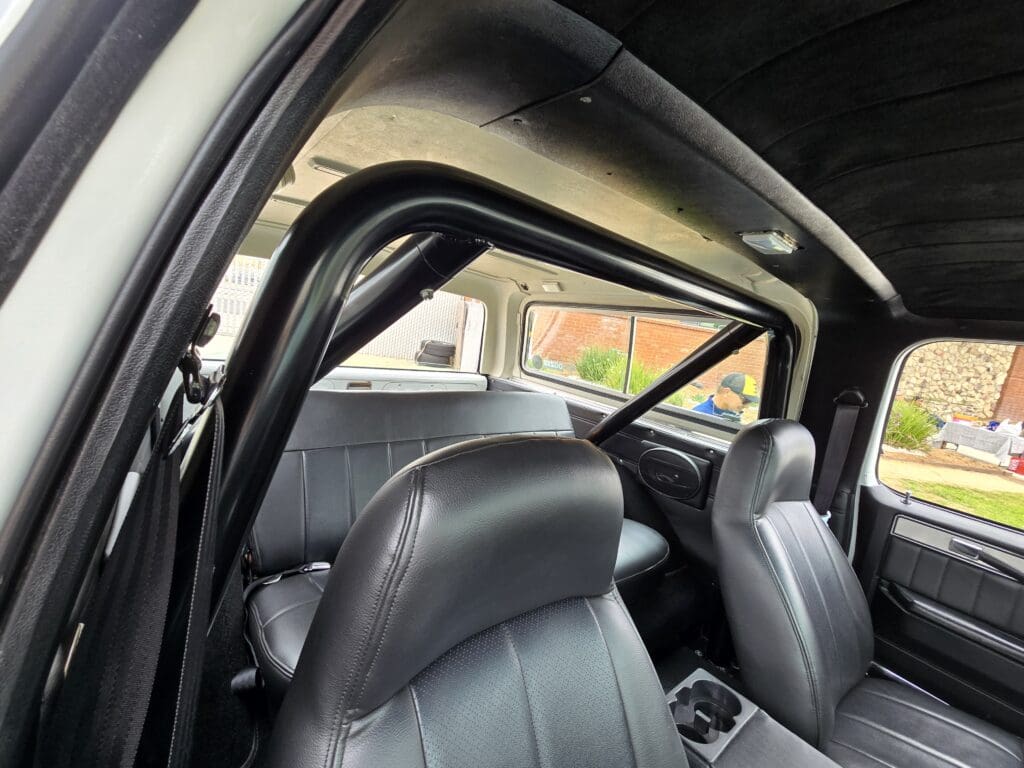Interior view of a car showing black leather seats and a roll cage.