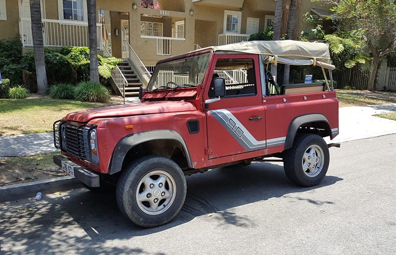 Red vintage off-road vehicle parked on a sunny street.
