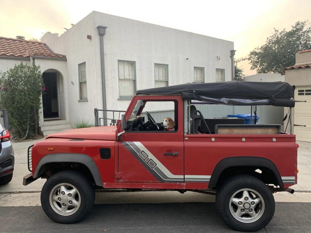 Red and white classic off-road vehicle parked near a building.