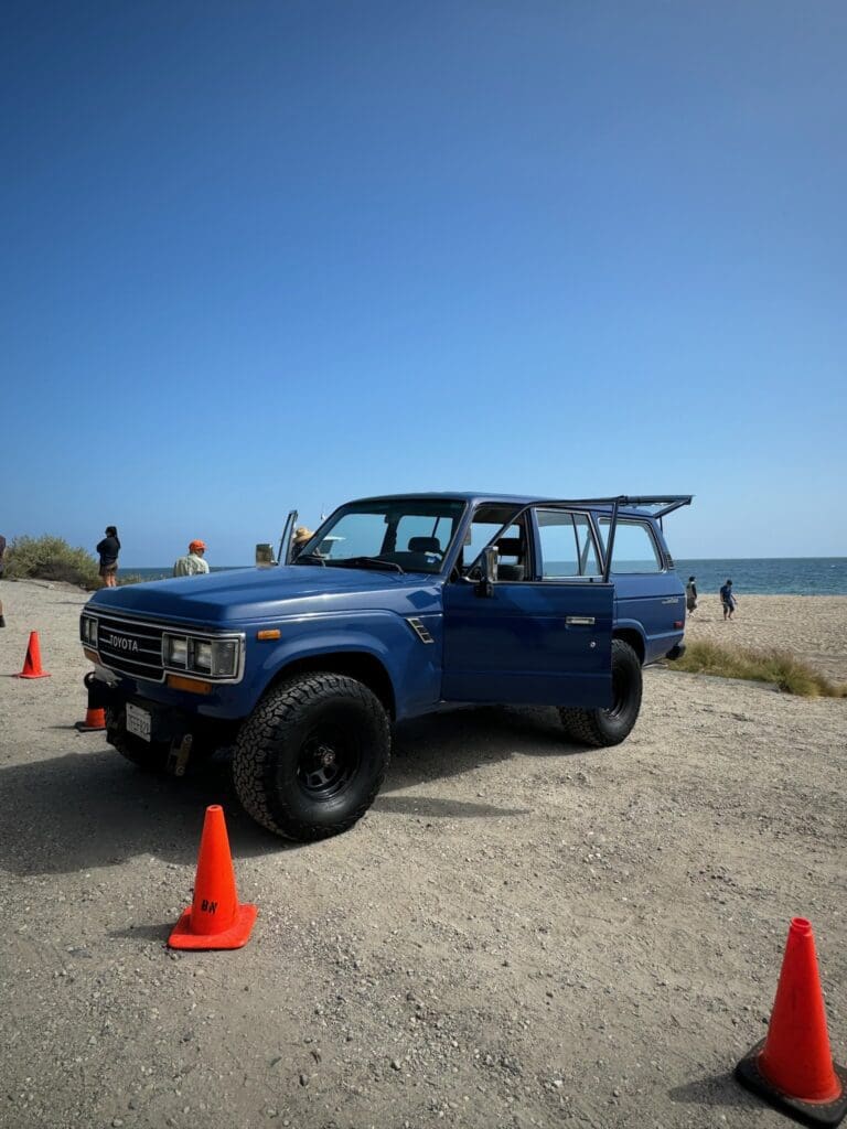Blue off-road vehicle parked near the beach with orange cones.