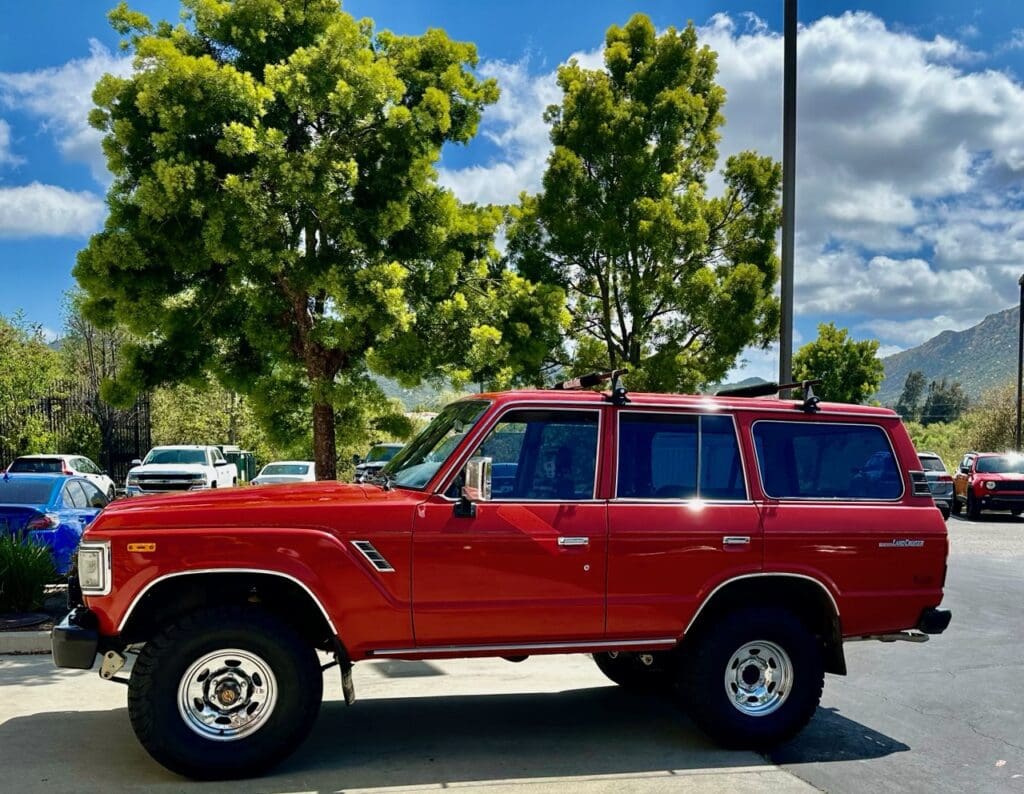 Classic red off-road SUV parked under trees on a sunny day.