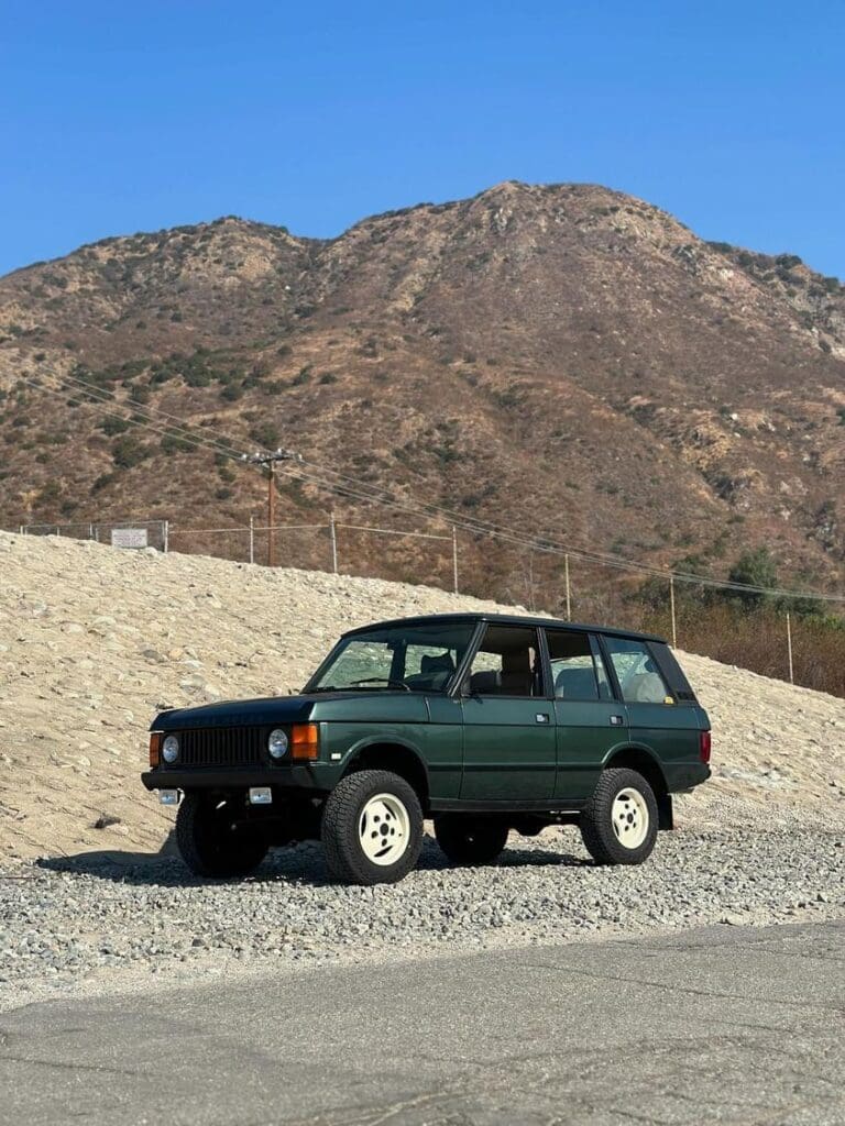 A green off-road vehicle parked on rocky terrain with a mountain in the background.