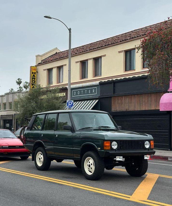 A classic black SUV parked on a city street with buildings in the background.