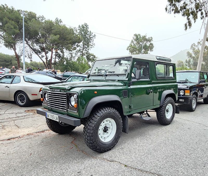 Green off-road vehicle parked in a lot with other cars.