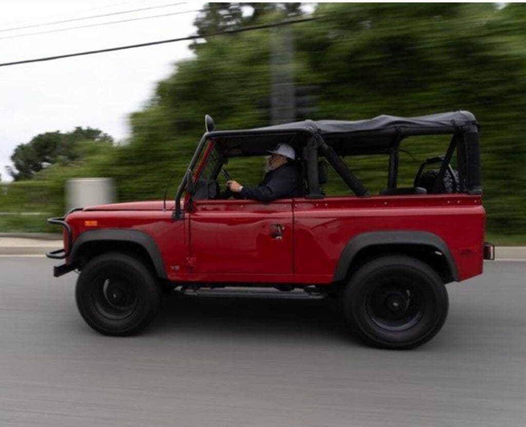 A red off-road vehicle driving on a road with a blurred background.