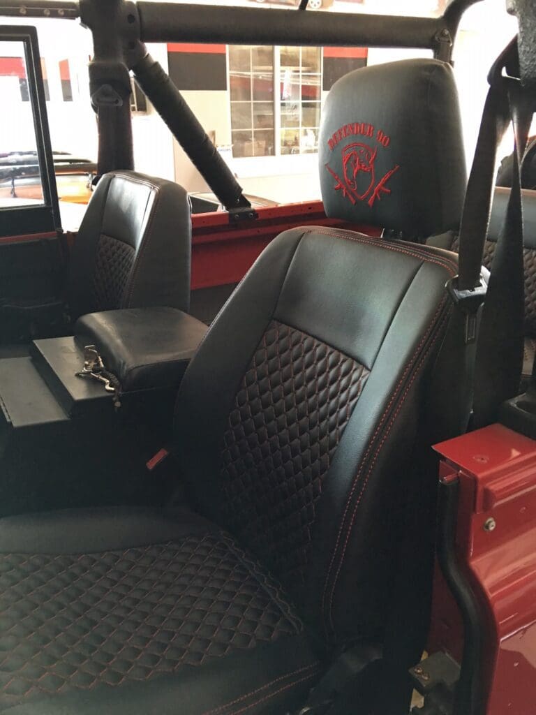 Close-up of a black leather car seat with red stitching.