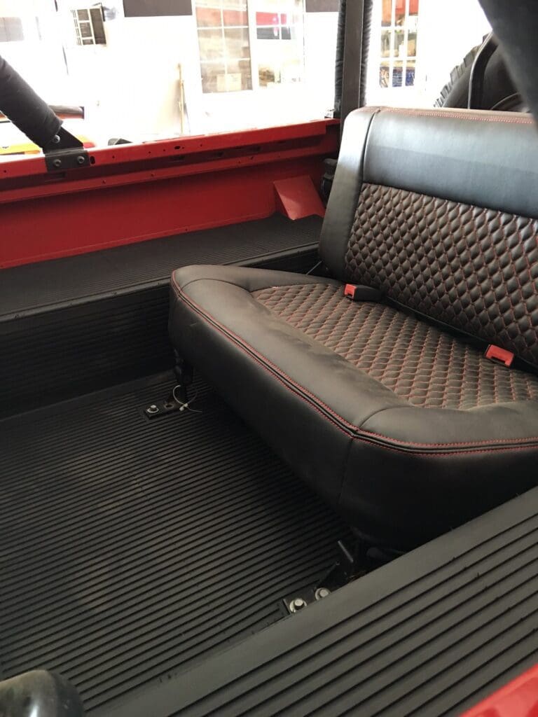 Interior view of a vehicle's back seat with patterned upholstery and black floor mat.