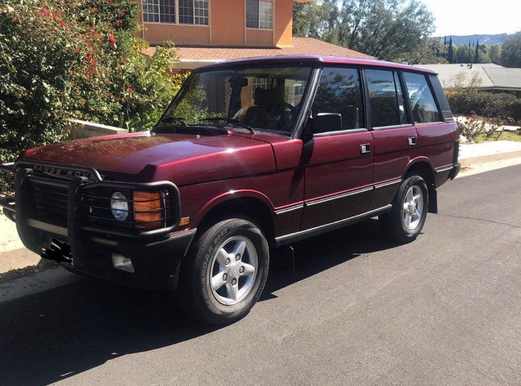 A maroon classic SUV parked on a sunny street.