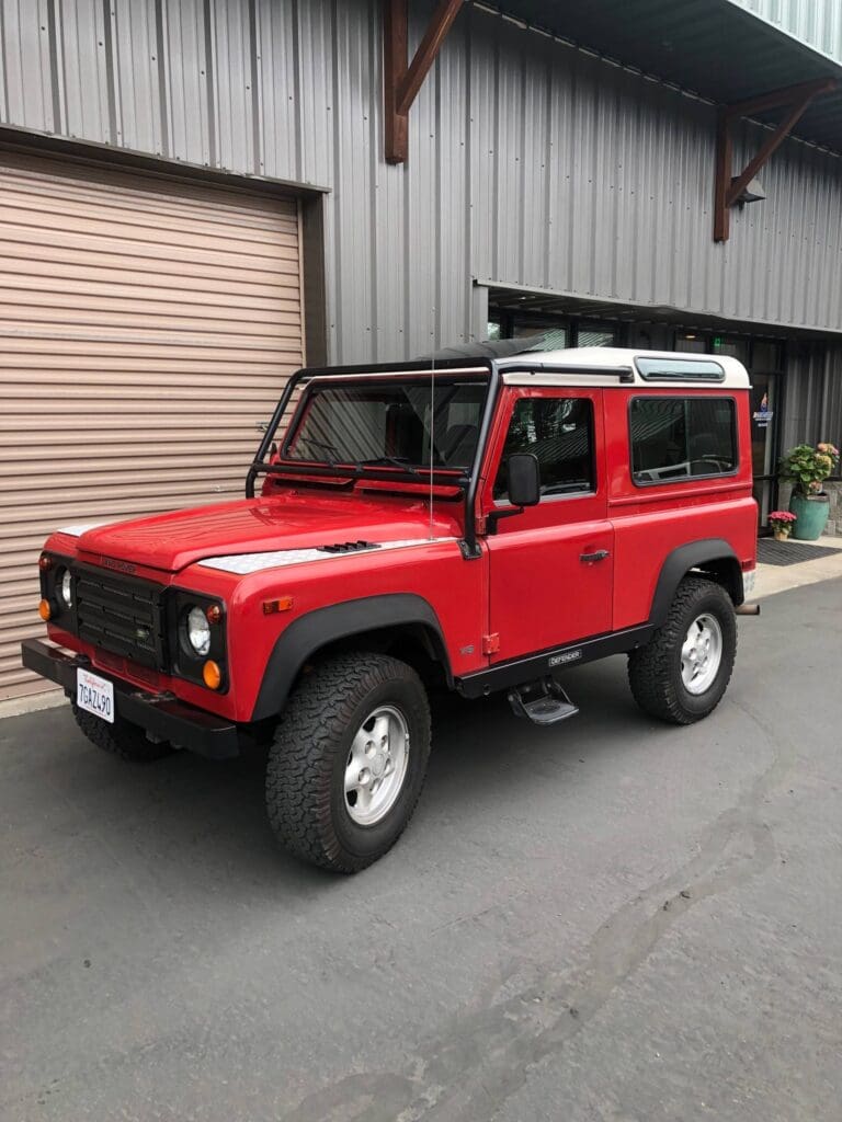 Red classic Land Rover Defender parked outside a garage.