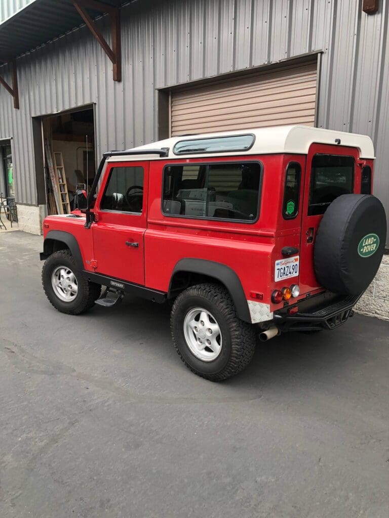 Red classic Land Rover Defender parked outside a garage.