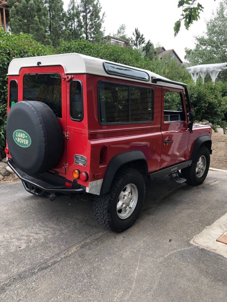 Red classic Land Rover Defender parked outside a garage.