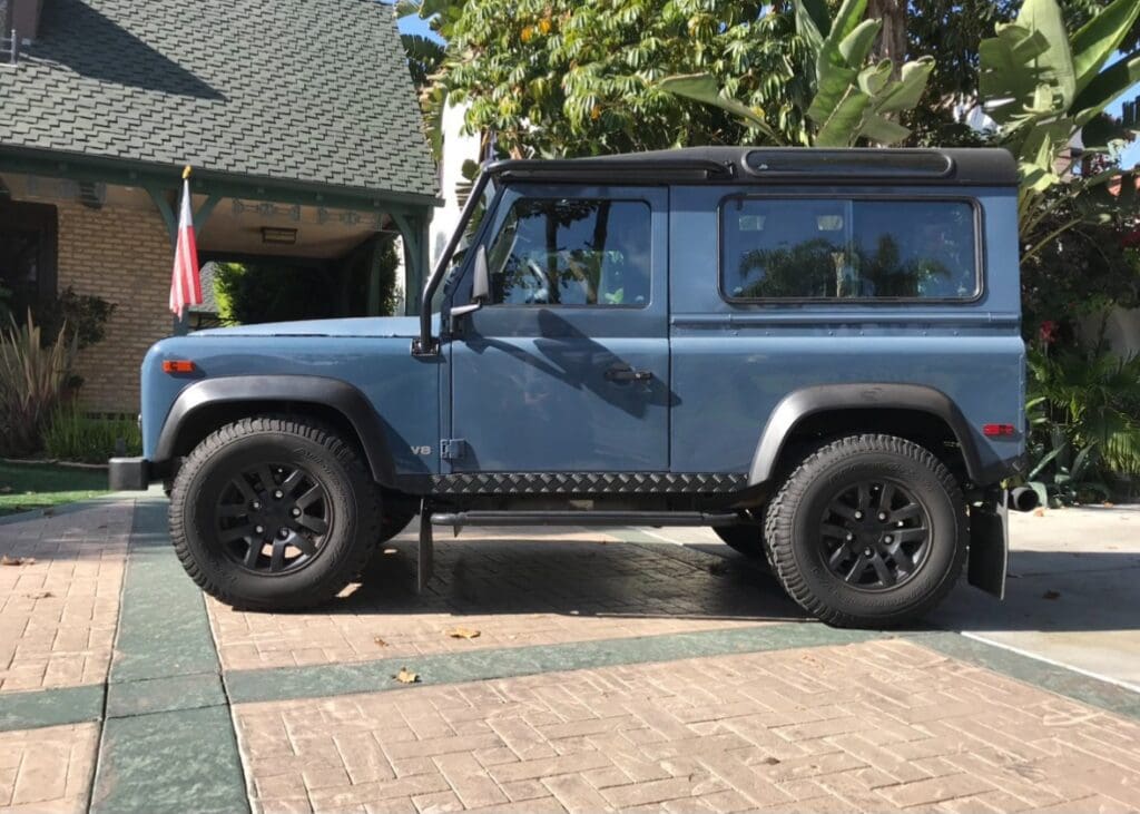 Blue off-road vehicle parked on a driveway with trees in the background.