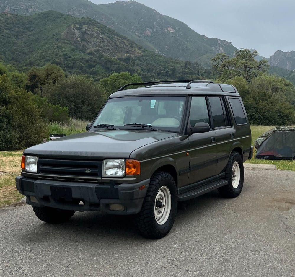 A dark green SUV parked on a road with mountains in the background.