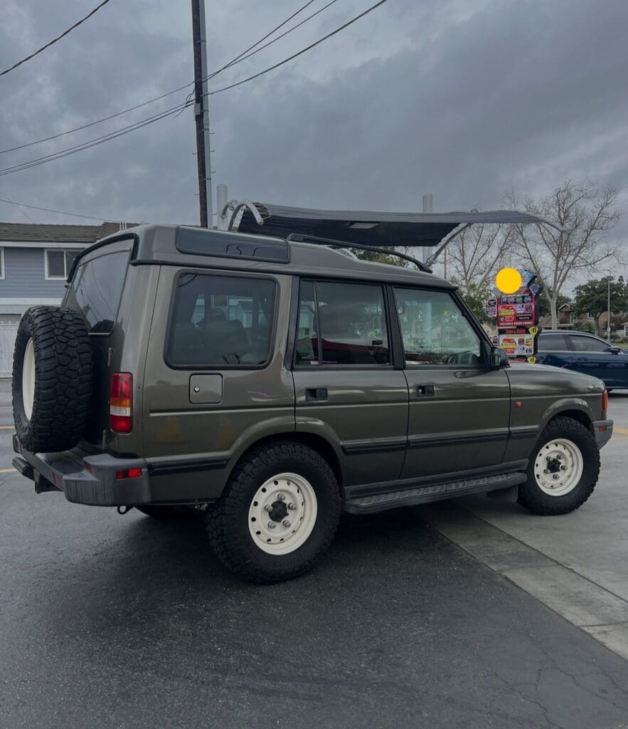 Dark green SUV parked on a wet street under cloudy skies.