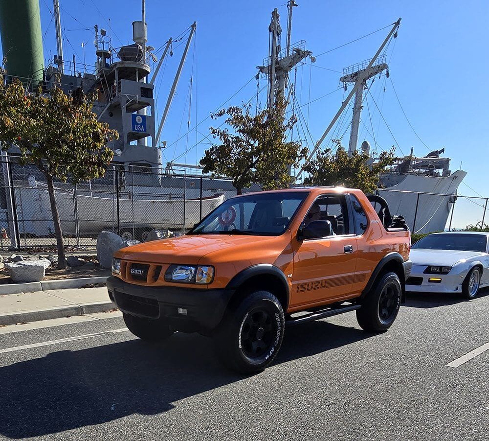 Orange Nissan pickup truck parked near a harbor with cranes.