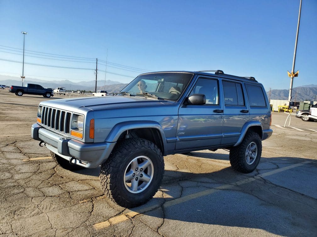 Blue Jeep Cherokee parked on cracked pavement under clear sky.