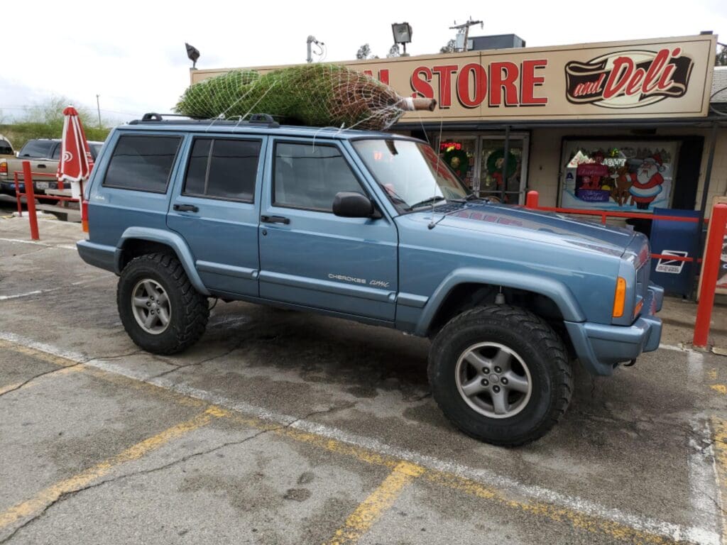 Blue Jeep parked outside a store with a roof rack.