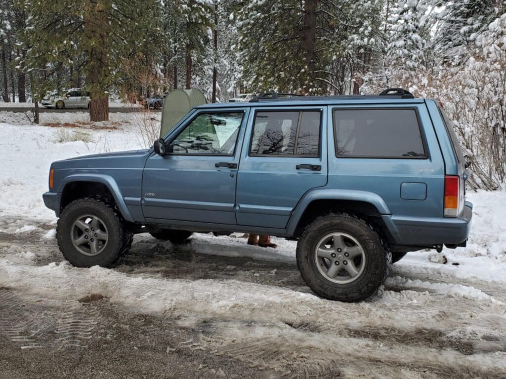 Blue SUV parked on snowy ground in a wooded area.
