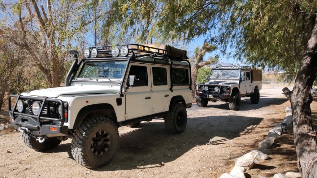 Two rugged off-road vehicles parked on a dirt path under trees.