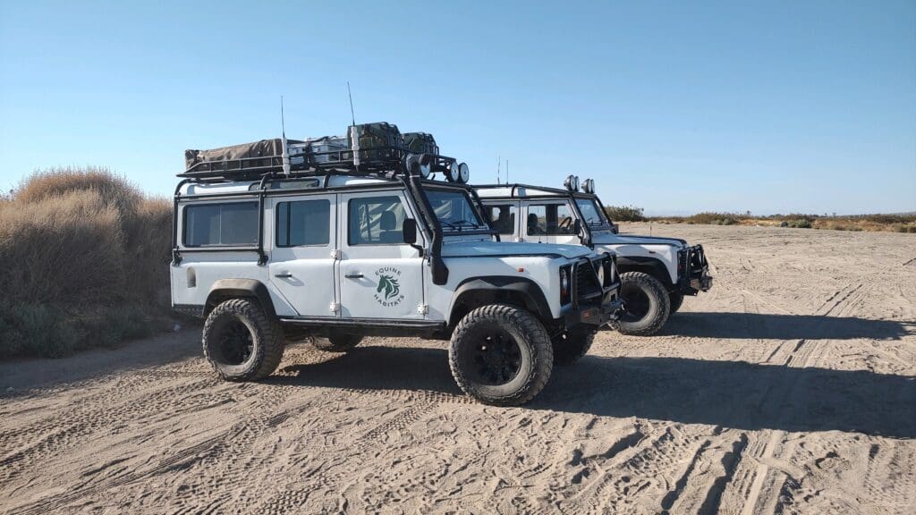 Three off-road vehicles parked on sandy terrain under a clear sky.