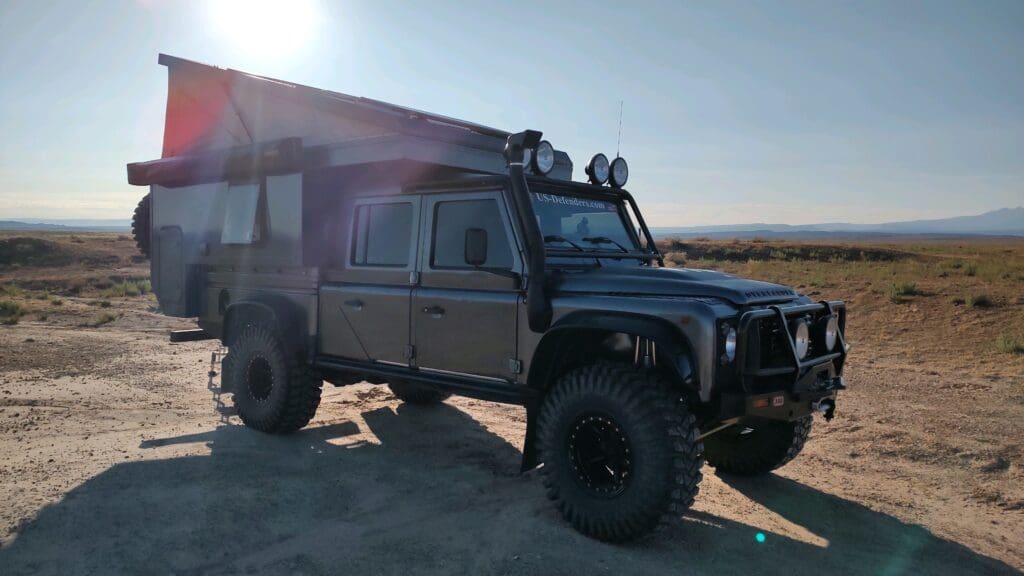A rugged off-road vehicle with large tires and roof lights at sunset.