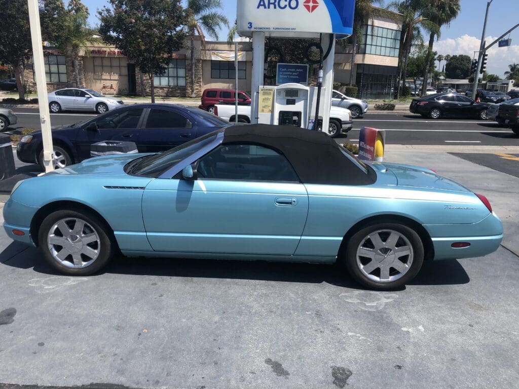Light blue convertible car parked at a gas station.