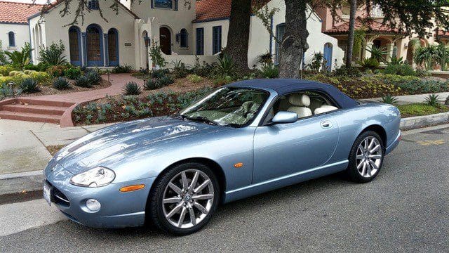 A sleek light blue convertible sports car parked in front of a stylish house.