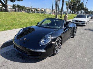 Black Porsche convertible parked on a sunny street near palm trees.