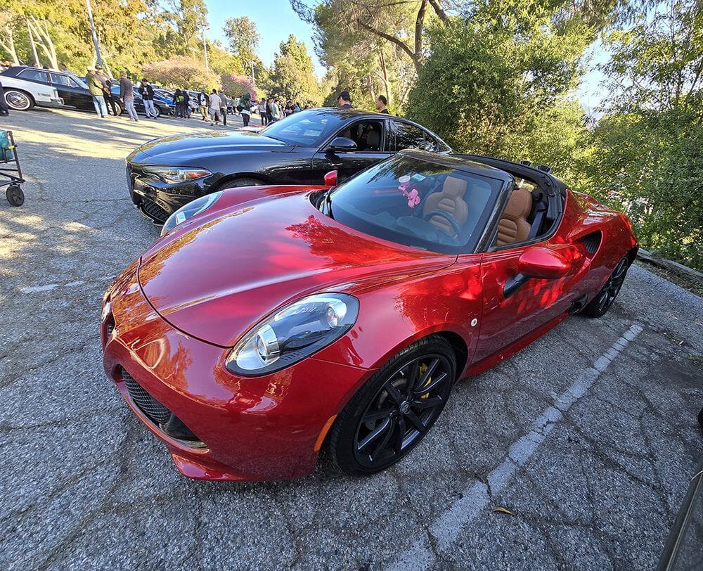 Red convertible sports car parked beside a black car on a sunny day.