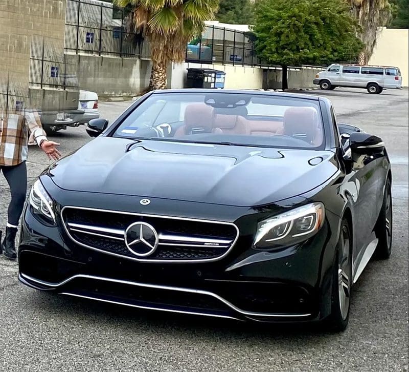 Black Mercedes convertible parked on a street with palm trees.