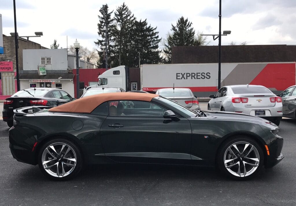 A dark convertible car with a tan soft top parked near a truck.