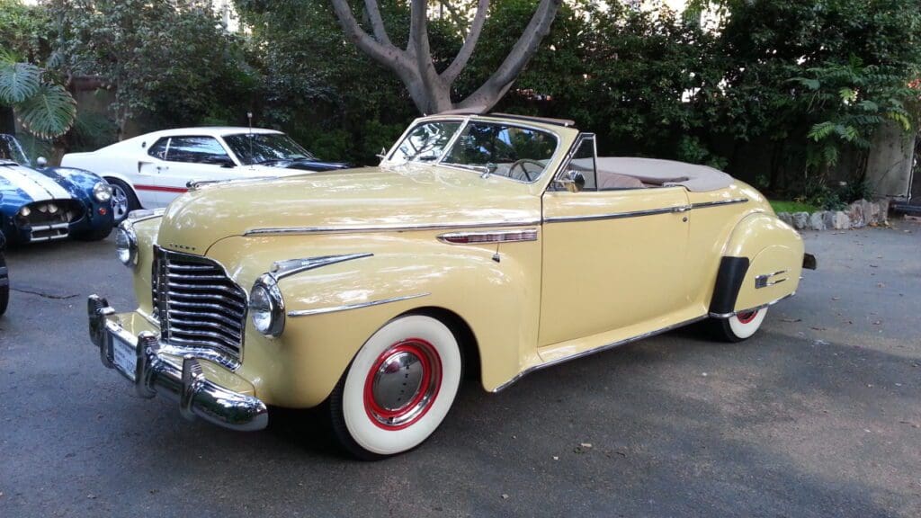 Vintage yellow convertible car parked outdoors beside trees.