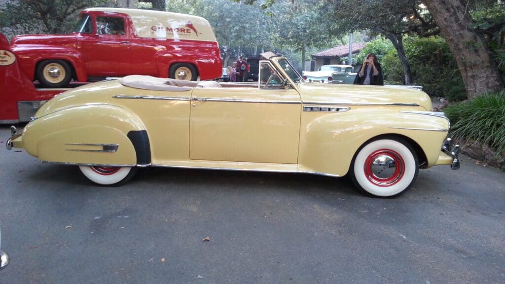 Classic yellow convertible car parked outdoors with red and white tires.