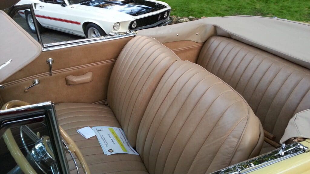 Interior of a vintage car with tan leather seats and a white classic car in the background.