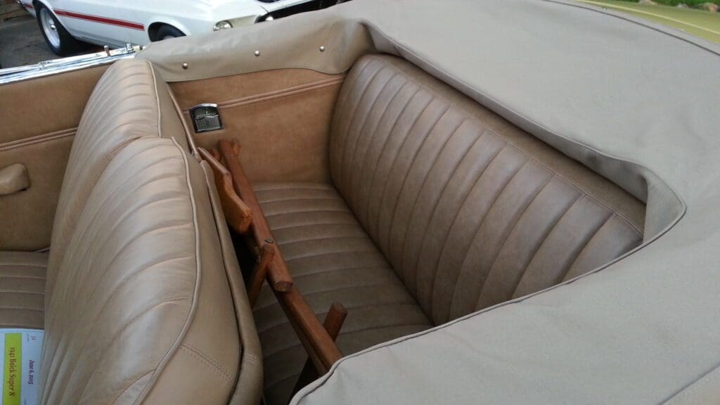 Vintage car backseat with brown leather upholstery and wooden armrest.