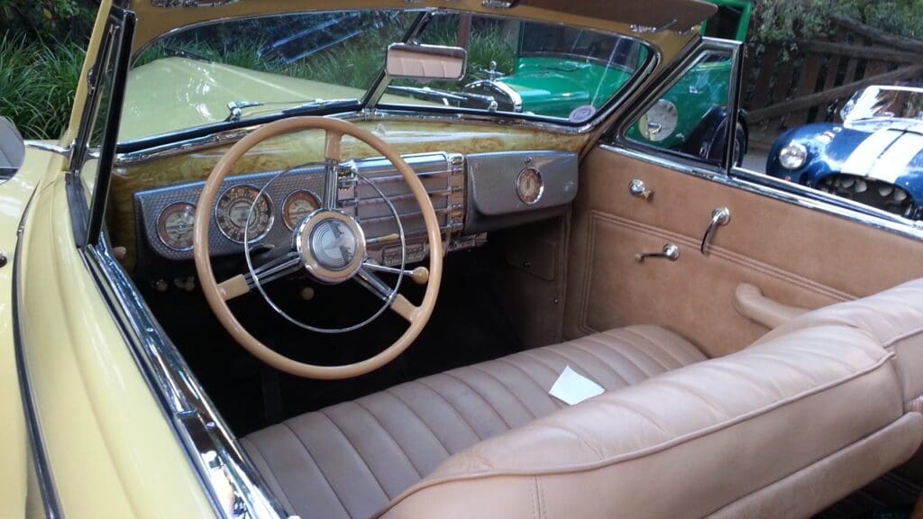 Interior of a vintage car with a classic steering wheel and brown leather seats.