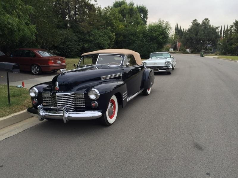 Classic black vintage car parked on a suburban street with trees and houses.