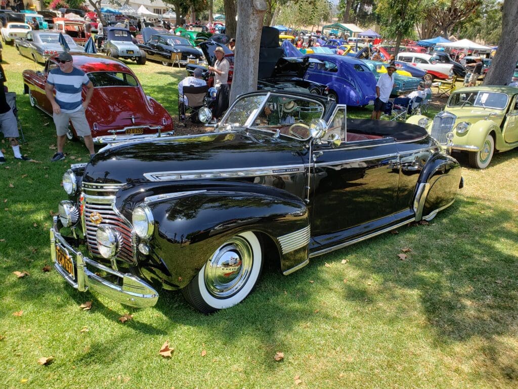 A shiny black vintage convertible car parked on grass at a car show.