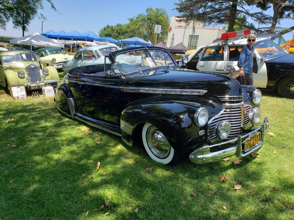 Classic black vintage car parked on grass at a sunny outdoor event.