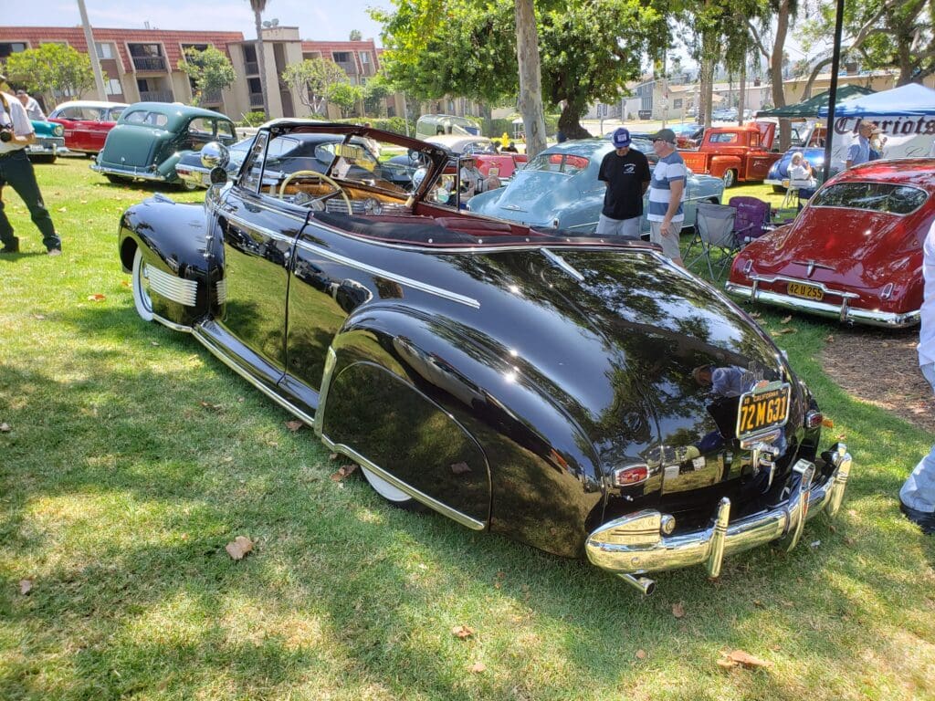 Classic black vintage car parked on grass at outdoor event.