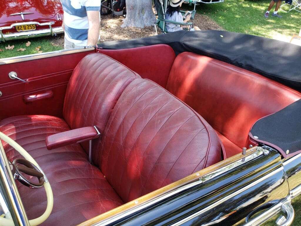 Vintage car's red leather interior with bench seats and an armrest.