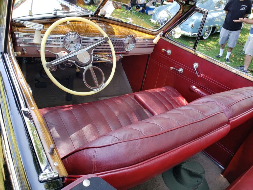 Vintage car interior with red leather bench seat and wooden dashboard.