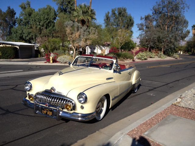 Classic cream-colored convertible car parked on a sunny suburban street.
