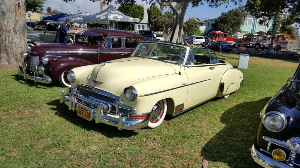 Classic cream convertible car parked on grass at a car show.