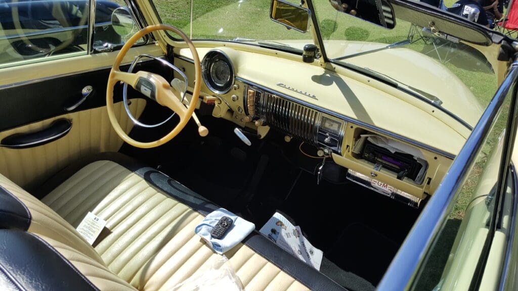 Classic car interior with beige leather seats and wooden steering wheel.