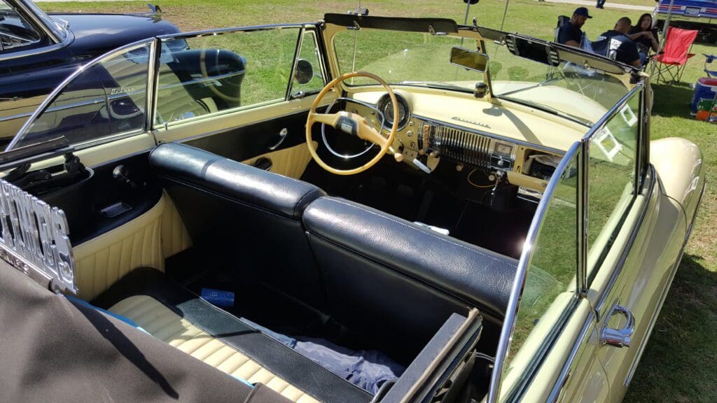 Vintage car interior with black leather seats and wooden steering wheel.