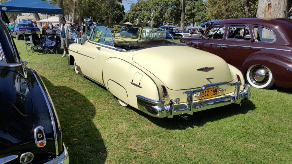 A classic cream-colored convertible car parked on grass at a car show.
