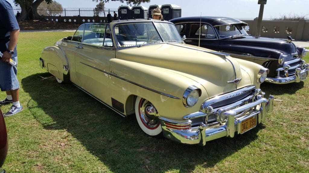 Classic yellow convertible car parked on grass at a vintage car show.