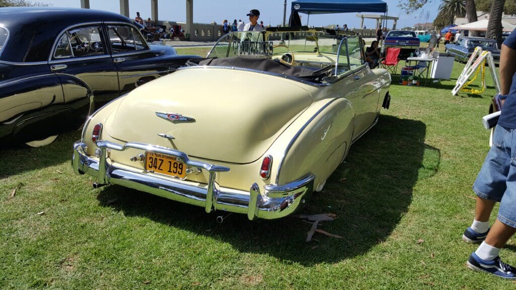 Classic yellow convertible car parked on grass at a vintage car show.